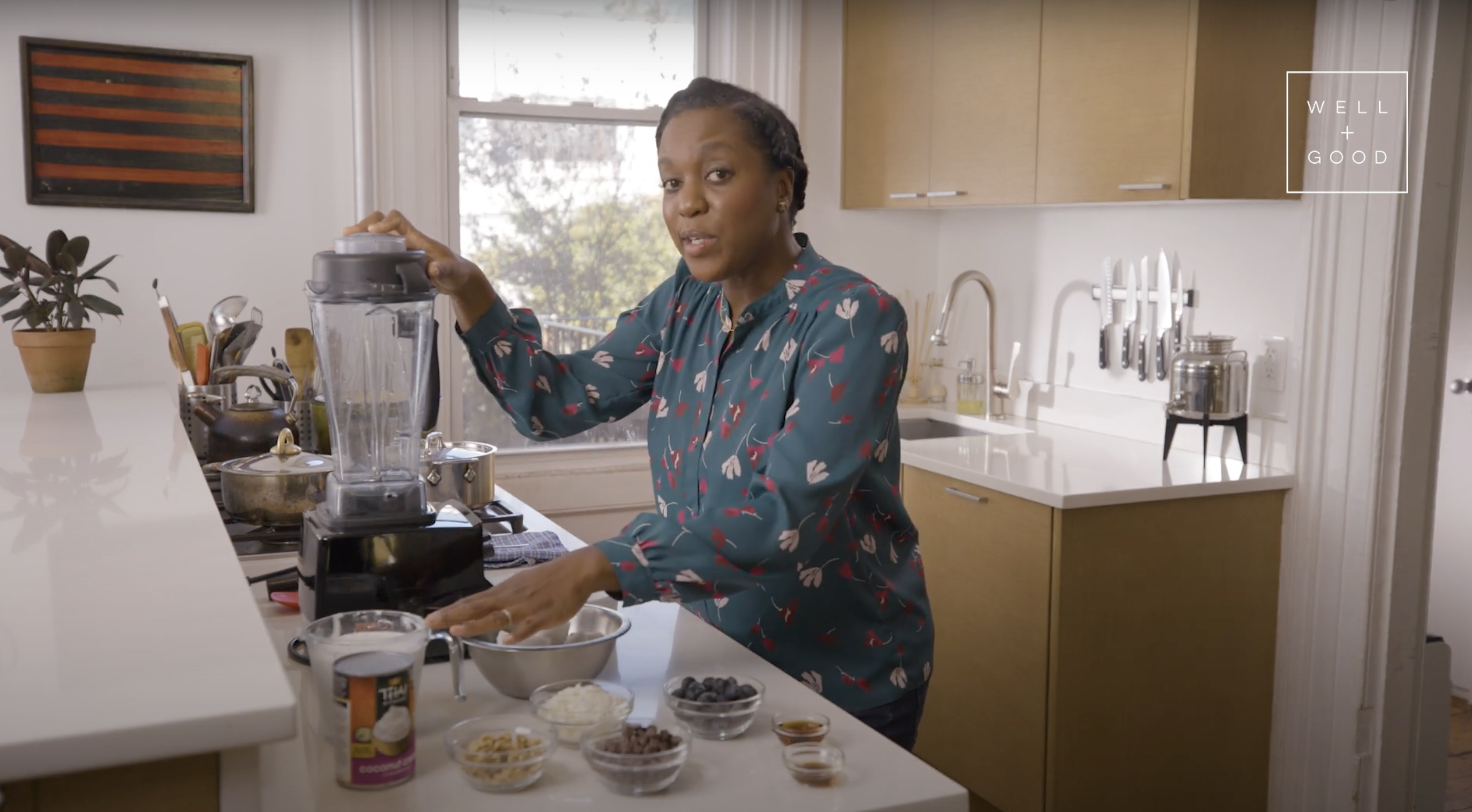 Maya Feller preparing a Coconut Smoothie Bowl in her kitchen with ingredients including coconut milk, blueberries, walnuts, chocolate chips, and vanilla.