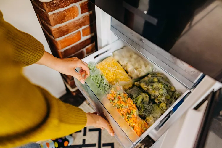 An organized freezer containing labeled containers of frozen spinach, homemade stock, fruits, nuts, meats, and pre-made meals.